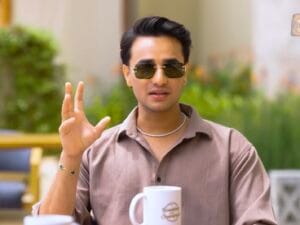 अभिषेक शर्मा हल्की भूरे रंग की शर्ट और धूप का चश्मा पहने बाहर बैठकर बातचीत करते हुए।