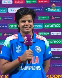 भारतीय महिला क्रिकेटर शेफाली वर्मा नीली जर्सी में मुस्कुराते हुए इंटरव्यू के दौरान माइक पकड़े हुए।