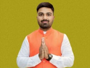 Manish Kashyap, जिसने सफेद कुर्ते के ऊपर नारंगी रंग की नेहरू जैकेट पहनी है। वह हाथ जोड़कर नमस्ते की मुद्रा में कैमरे की ओर देख रहे है और कलाई में घड़ी बंधी है।