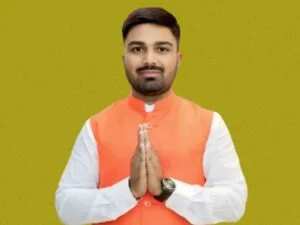 Manish Kashyap, जिसने सफेद कुर्ते के ऊपर नारंगी रंग की नेहरू जैकेट पहनी है। वह हाथ जोड़कर नमस्ते की मुद्रा में कैमरे की ओर देख रहे है और कलाई में घड़ी बंधी है।