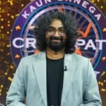 ग्रे सूट और काले टी-शर्ट में रवि गुप्ता KBC शो के मंच पर मुस्कुराते हुए खड़े हैं
